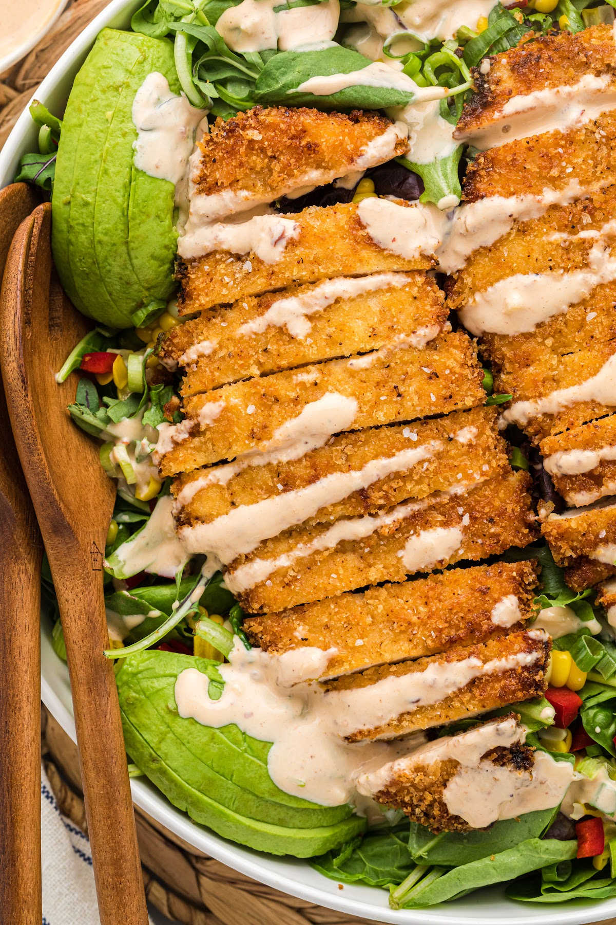 crispy fried chicken cutlets sliced and drizzled with chipotle dressing on a bed of mixed greens and vegetables.