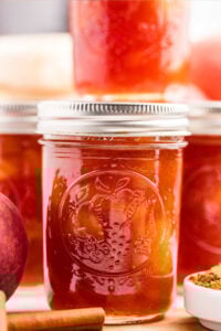 Close-up of jars filled with peach preserves, with cinnamon sticks in the foreground, showcasing the final product.