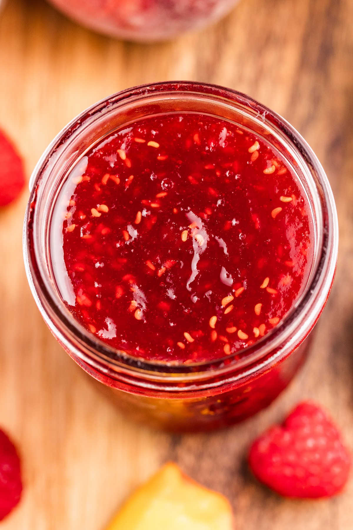Mason jars filled with raspberry peach jam surrounded by fresh peaches and raspberries.