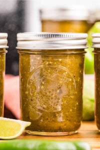 Close-up of a single jar of salsa verde with a lime wedge in front.