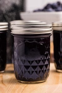 Multiple jars of blueberry syrup on a wooden surface.