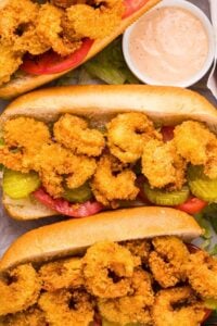 A close-up of a Shrimp Po’Boy sandwich showing the golden, crispy shrimp inside the bread with fresh toppings.
