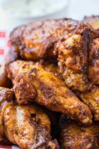 A pile of smoked chicken wings with a glossy, caramelized glaze, served on a checkered paper-lined basket.