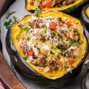 Individual serving of sausage stuffed acorn squash on a wooden plate, garnished with grated Parmesan and parsley.