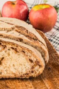 front shot of inside of bread sliced up with apples in background.
