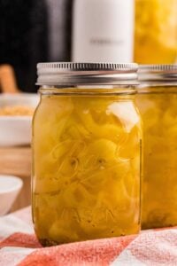sealed jar of banana peppers on red checkered cloth.