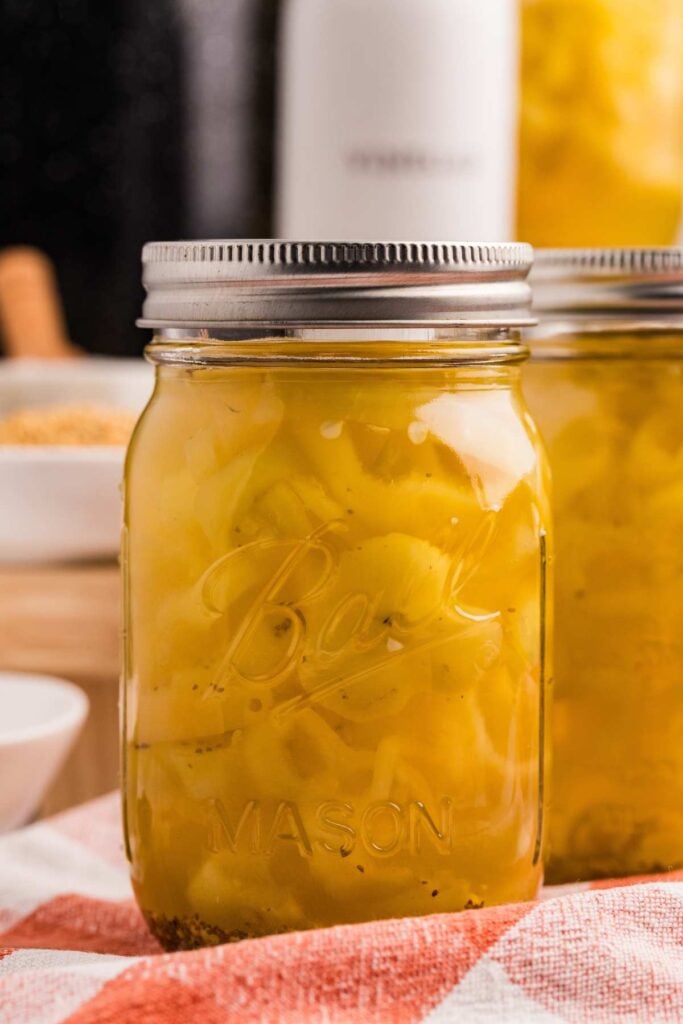 sealed jar of banana peppers on red checkered cloth.