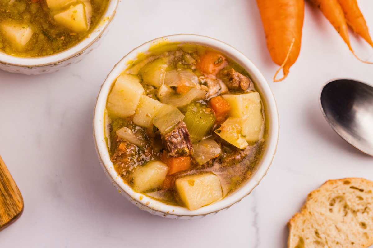 overhead shot of beef stew in bowl with carrots, bread, and a spoon on the edge.