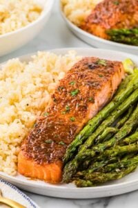 front shot of broiled salmon piece on plate in the middle of rice and asparagus.