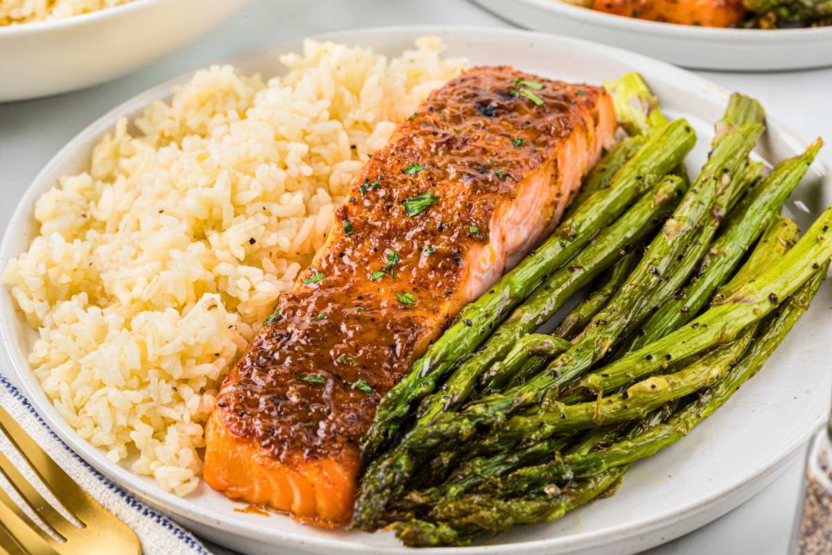 front shot of broiled salmon fillet on plate in the middle of rice and asparagus.