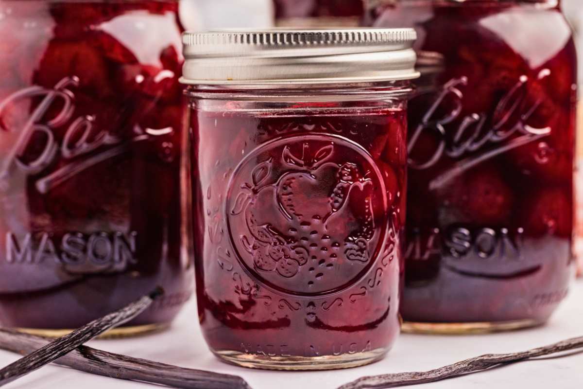 close up of small jar of bourbon cherries, with larger jars behind and vanilla beans in front.