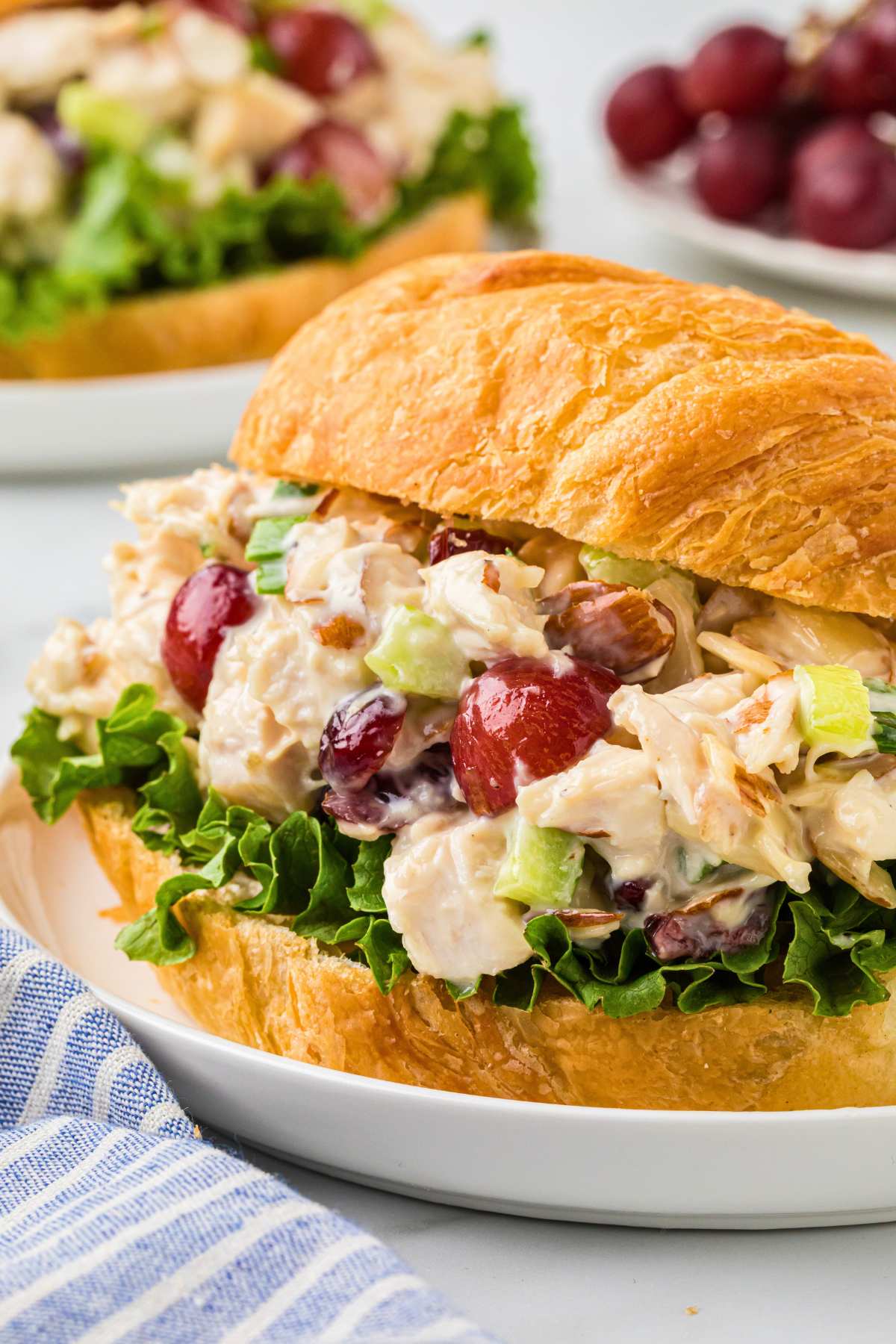 sideways shot of filled croissant sandwich on counter with grapes in background.