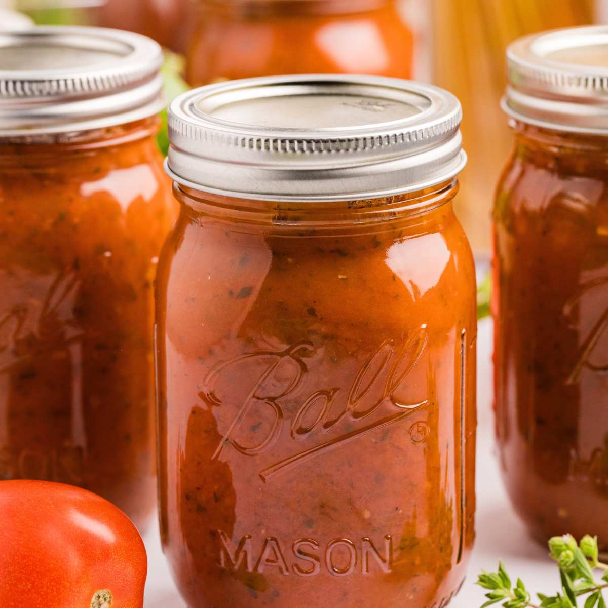 canned jars of spaghetti sauce on with tomato on side.