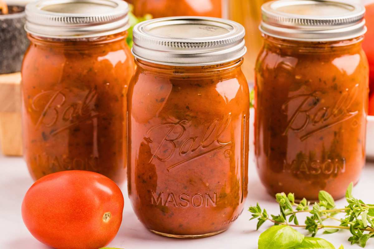 front image of three closed jars of canned spaghetti sauce with a tomato and parsley in front.