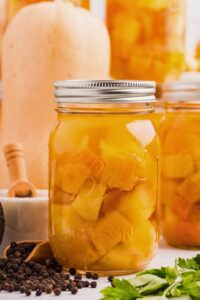 jar of butternut squash soup base, with peppercorns and herbs in front, and a butternut squash and other canned jars behind.