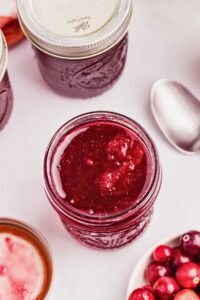 opened jar of cranberry sauce with cranberries and spoon on the side.