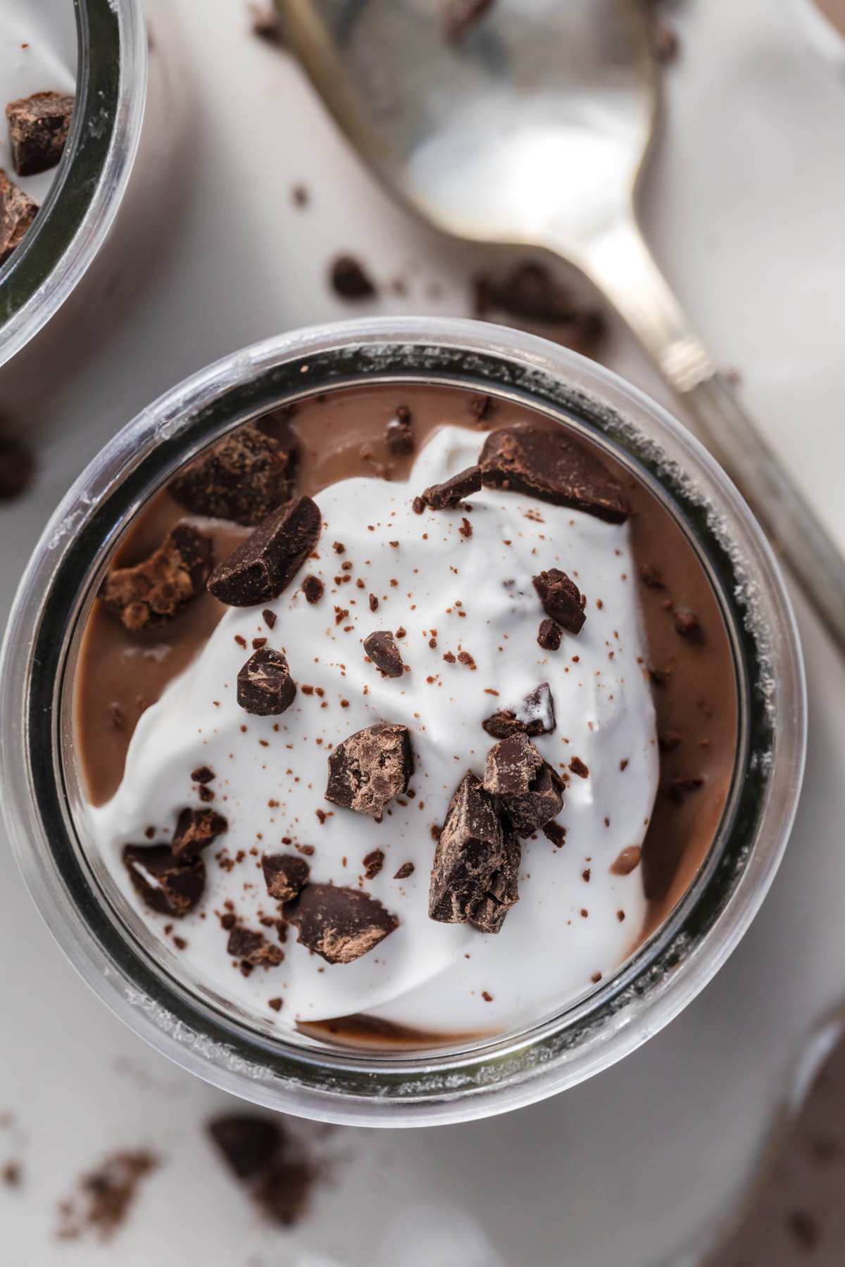top view of chocolate pudding with whipped cream and chocolate pieces in jar next to spoon.
