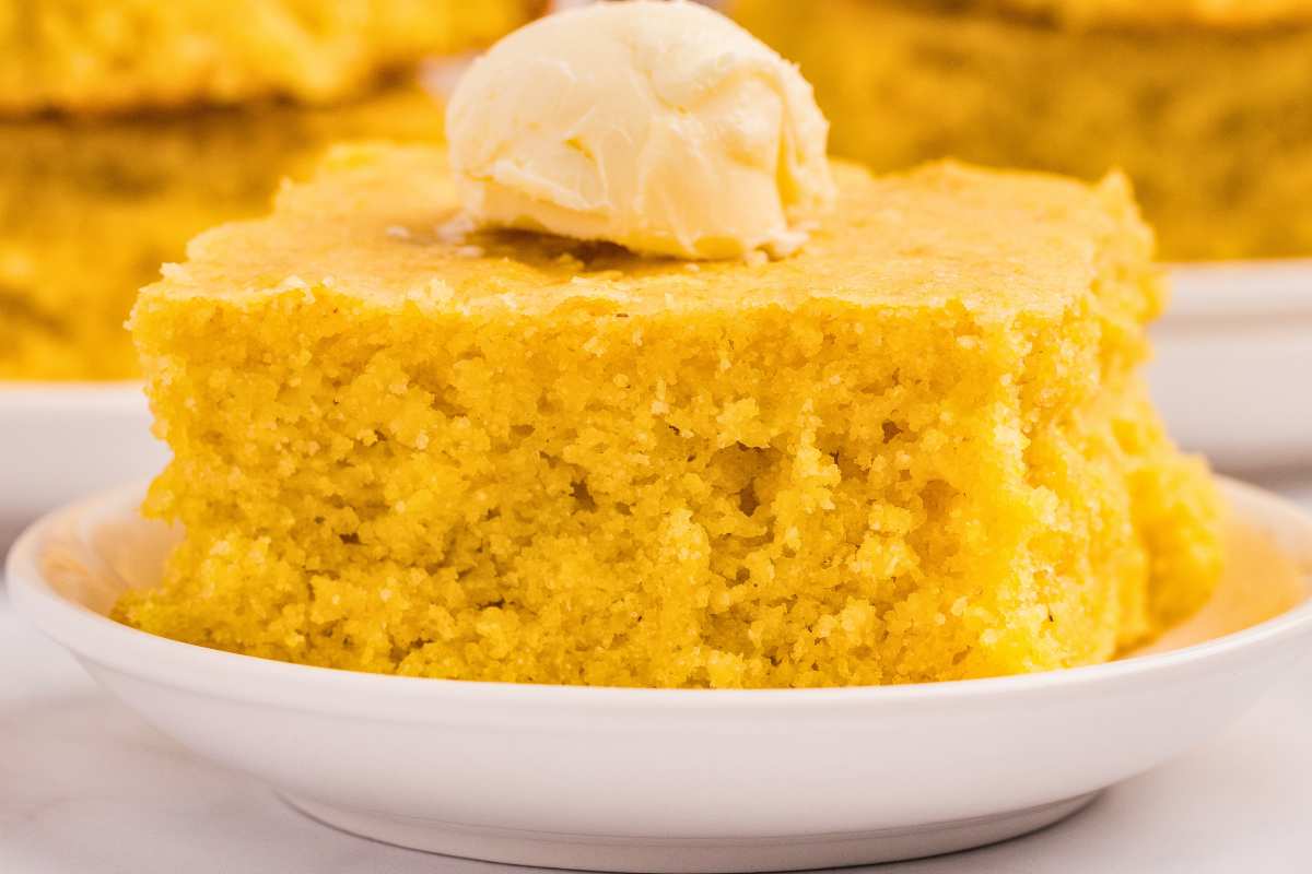 serving of cornbread on plate with pat of butter on top.