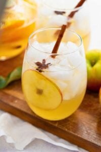 glass of fall prosecco sangria on wooden board with fruit slice and cinnamon stick inside.