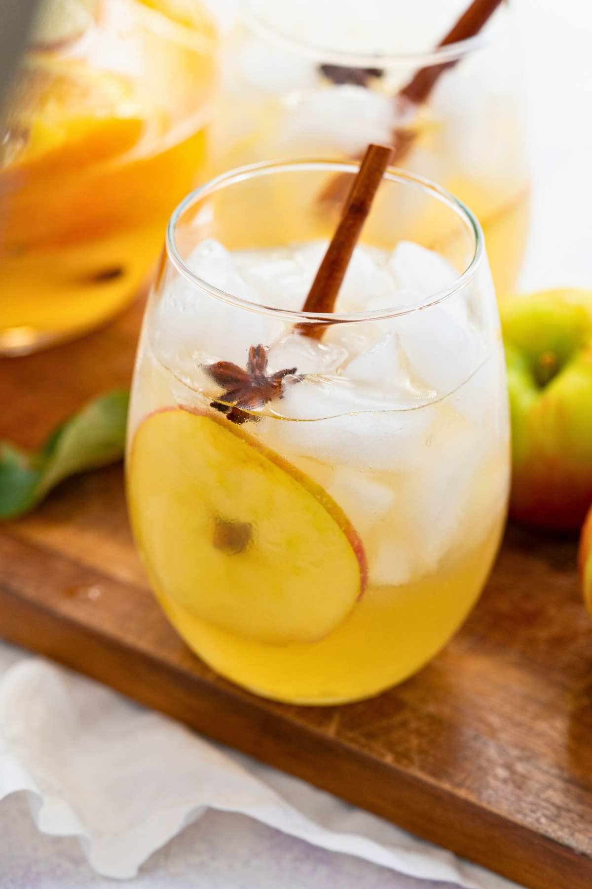 glass of fall prosecco sangria on wooden board with fruit slice and cinnamon stick inside.