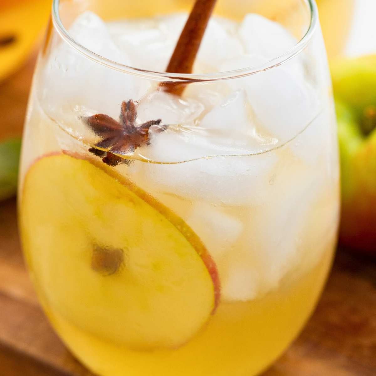 close up of glass of fall prosecco sangria with fruit slice and cinnamon stick inside.