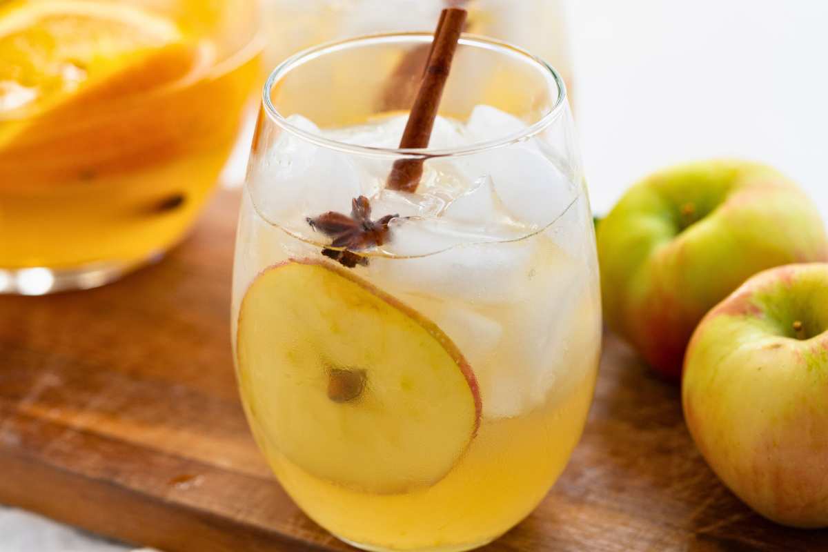 glass of sangria with fruit slice and cinnamon stick on wooden board with apples.