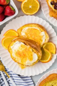 two French toast slices with cream cheese and orange sauce on plate with orange slices on side.