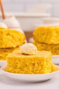 piece of cornbread on plate with butter on top, and other pieces in background.