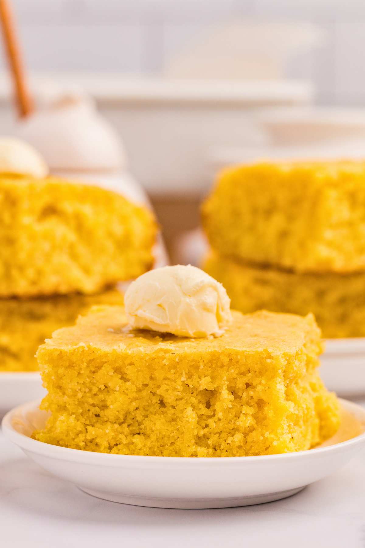 piece of cornbread on plate with butter on top, and other pieces in background.