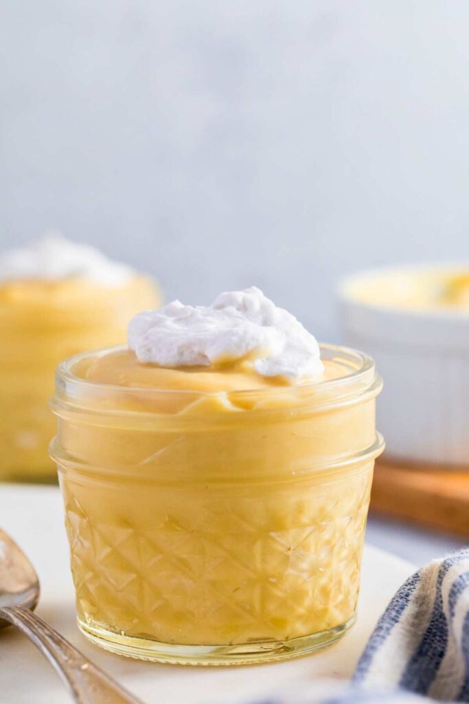 vanilla pudding in quarter pint glass jar with whipped cream on top, with another in background.
