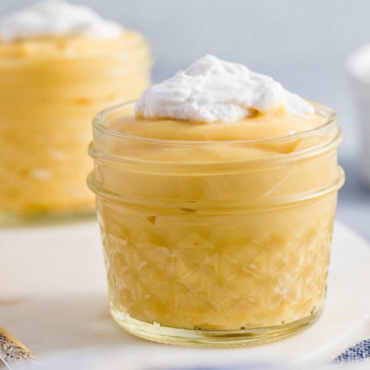 two vanilla puddings in quarter pint glass jars with whipped cream on top.