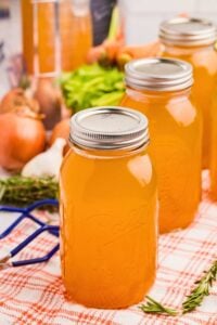 canned jars of vegetable stock lined up on cloth with vegetables behind.