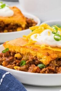 serving of casserole in bowl with cornbread and sour cream on top.