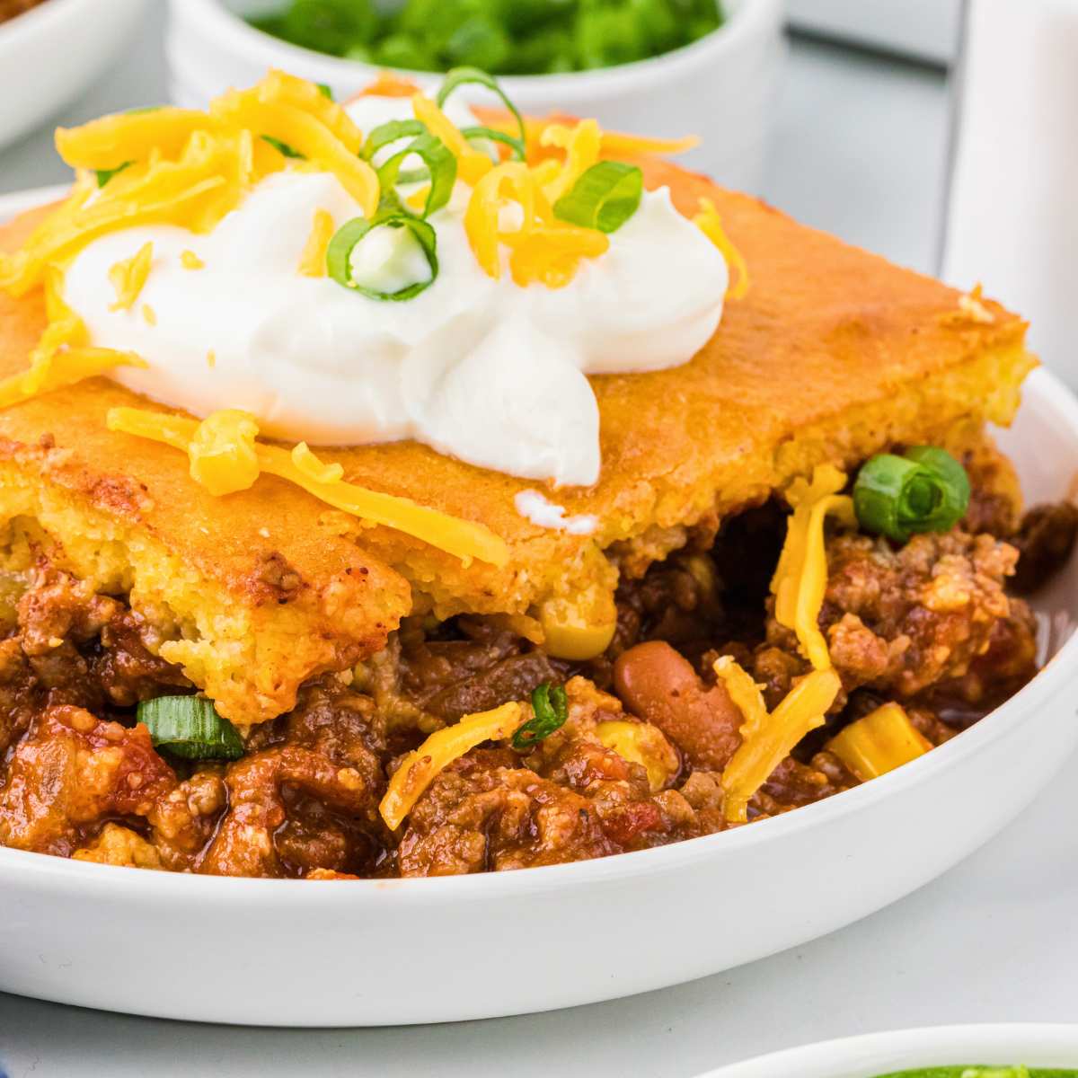 chili in bowl with cornbread and sour cream on top.