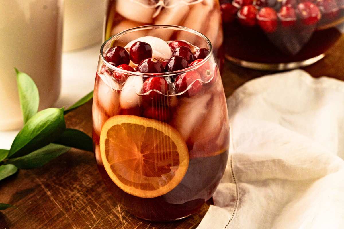 clear glass of christmas prosecco sangria with orange slice, cranberries, and ice inside.