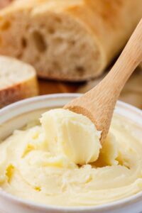 homemade butter in ceramic dish with wooden spoon scooping some out.