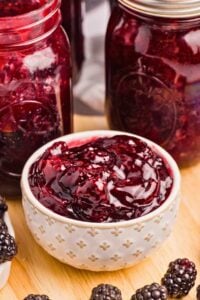 bowl of blackberry pie filling with jars behind.