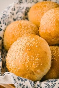 Italian sesame rolls resting on blue and white patterned cloth in basket.
