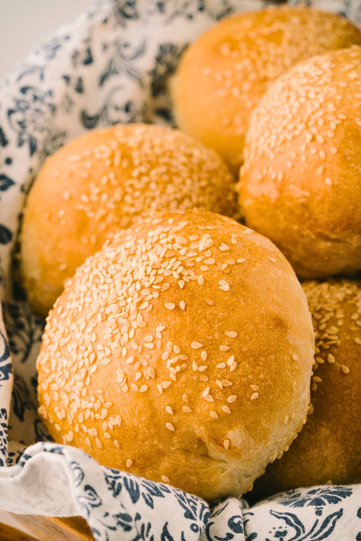 Italian sesame rolls resting on blue and white patterned cloth in basket.