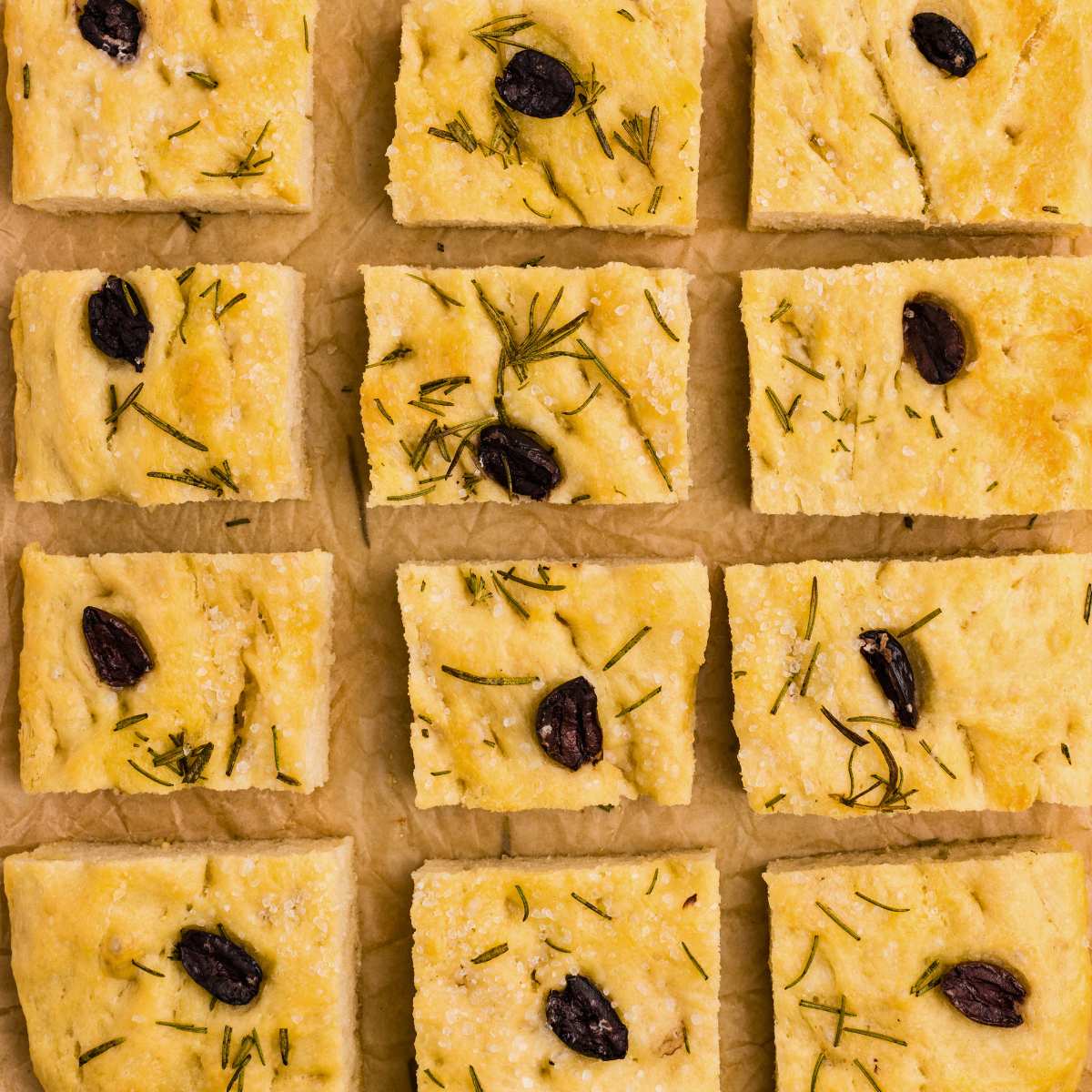 square pieces of focaccia bread topped with rosemary and olives.