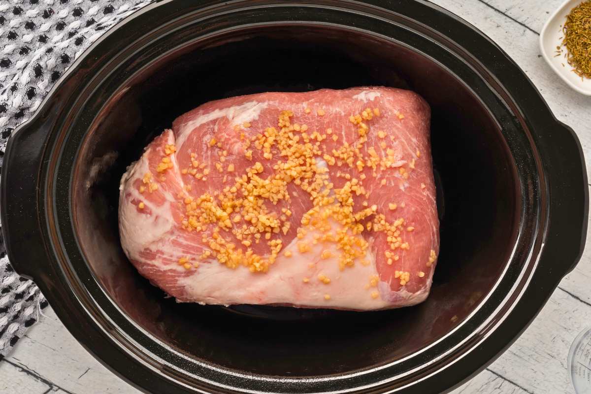 pork roast in slow cooker with garlic added on top.