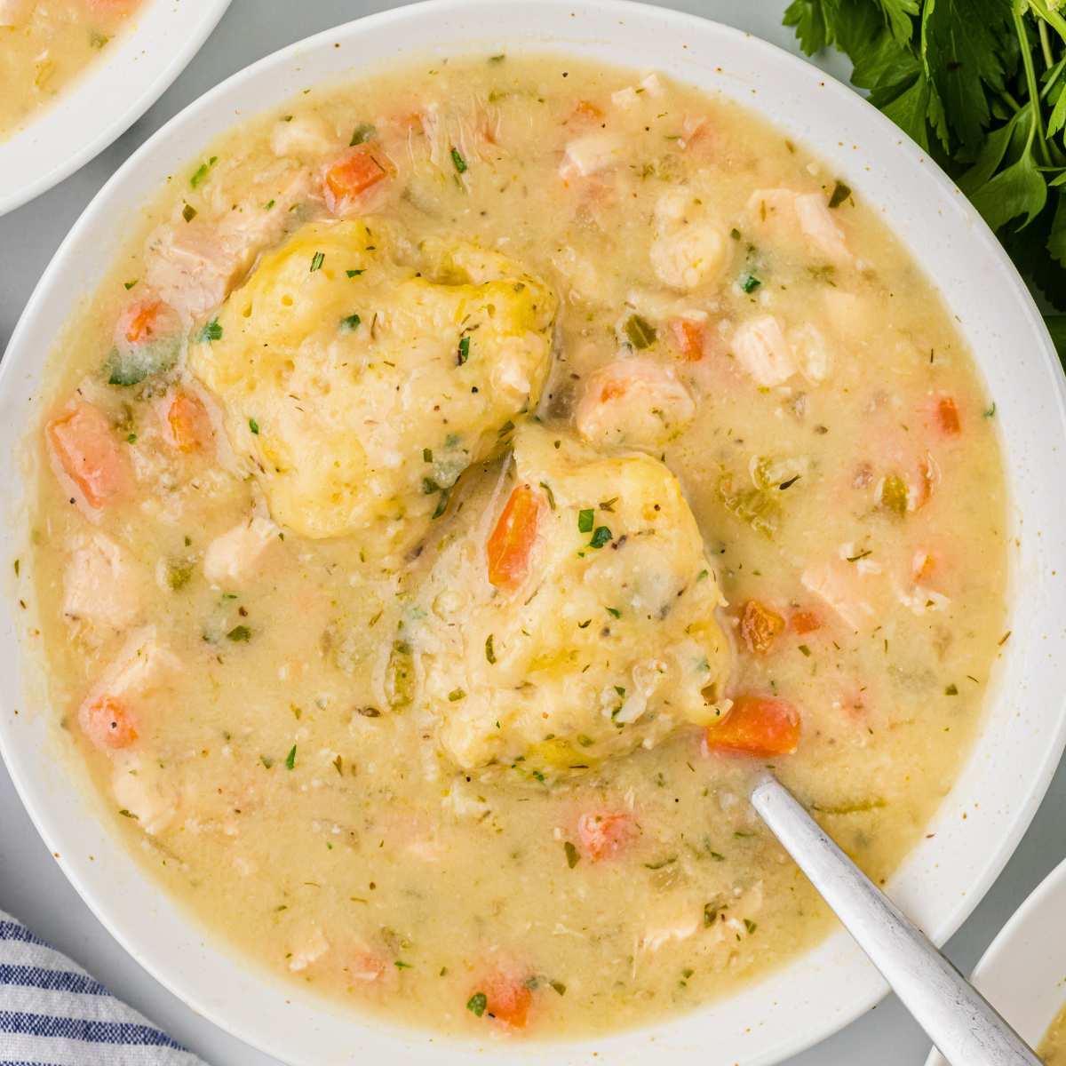 bowl of chicken soup with dumplings floating on top with spoon.
