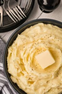 mashed potatoes in bowl with pat of butter with forks nearby.