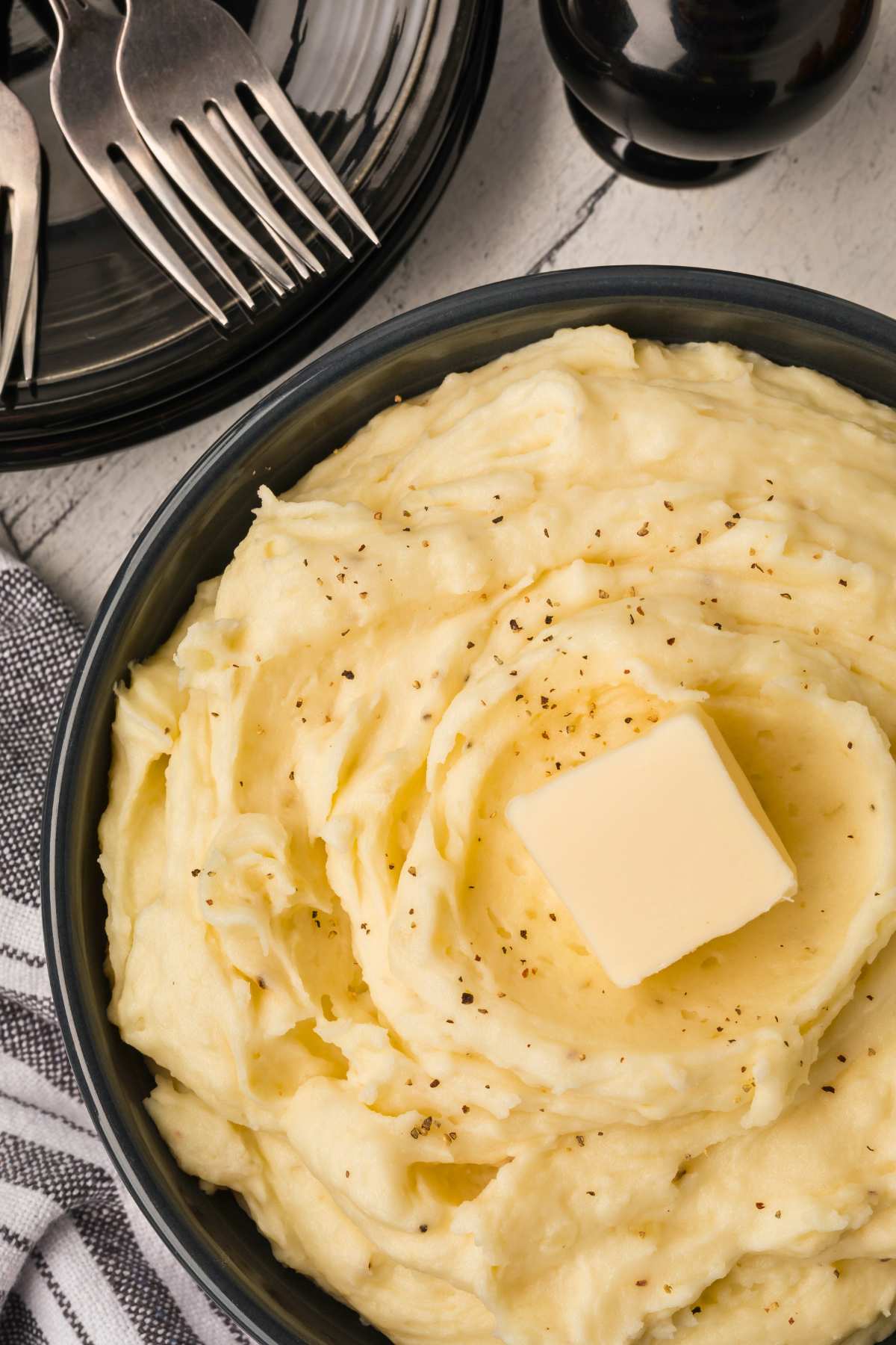 mashed potatoes in bowl with pat of butter with forks nearby.