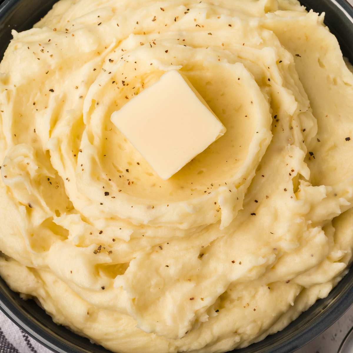 close up of mashed potatoes in bowl with butter square on top.