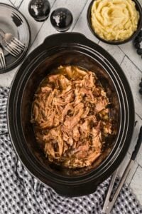 shredded pork roast in slow cooker on counter.