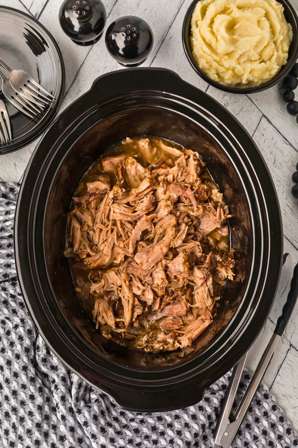 shredded pork roast in slow cooker on counter.
