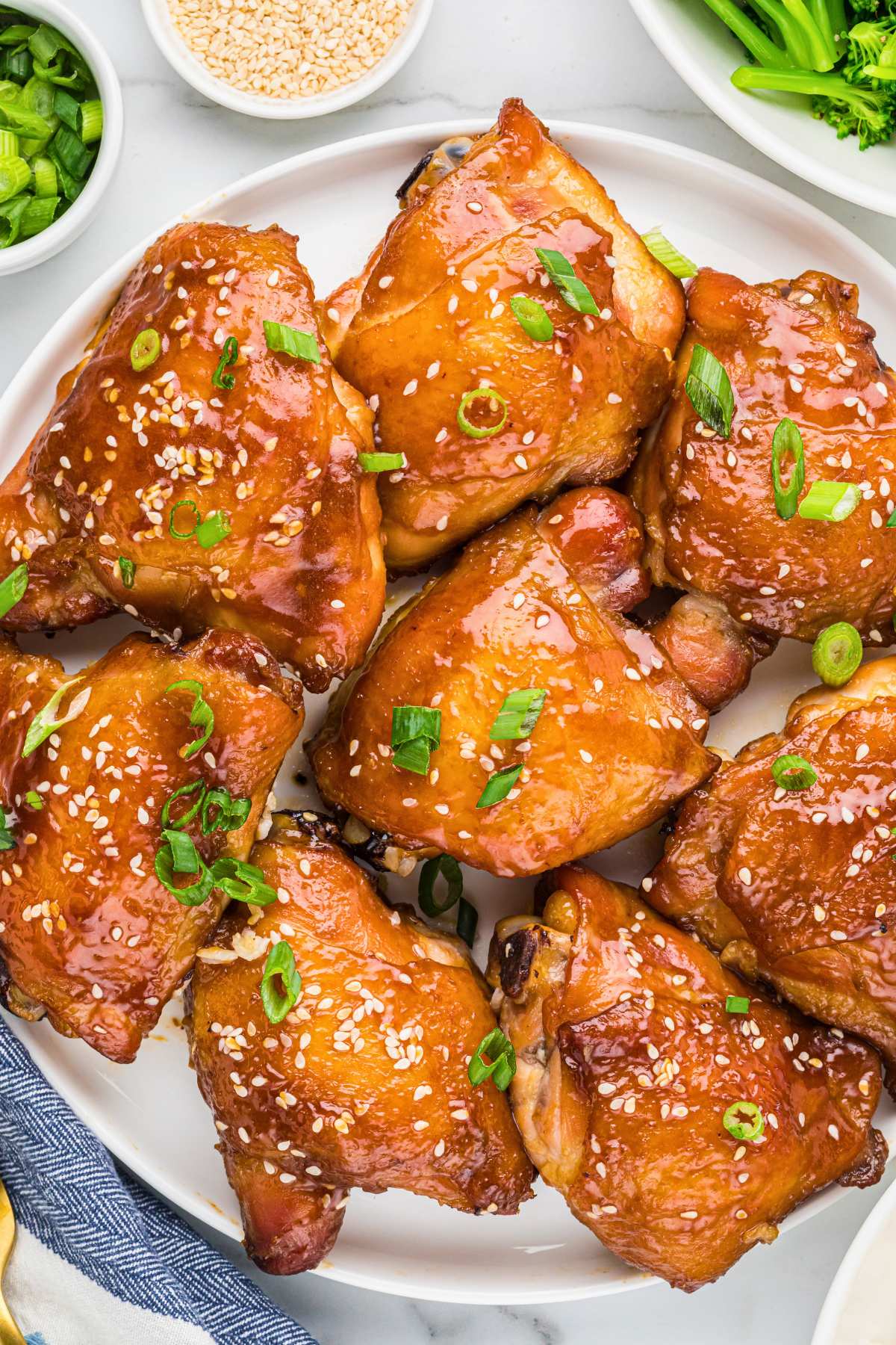 soy glazed chicken thighs on plate topped with sesame seeds and scallions.