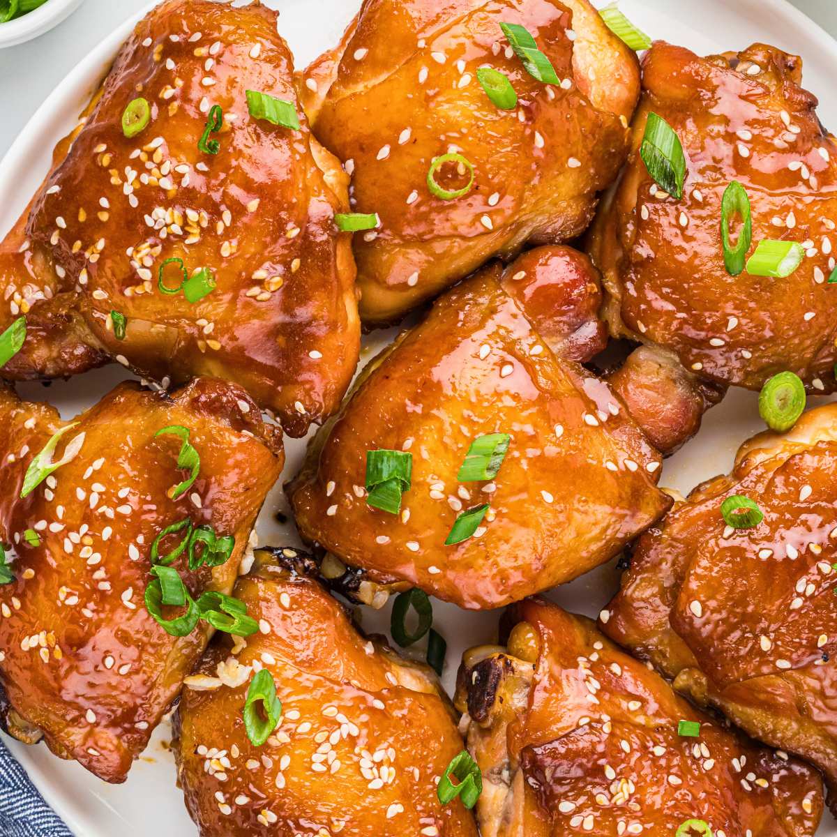 soy marinated chicken thighs on plate topped with sesame seeds and scallions.