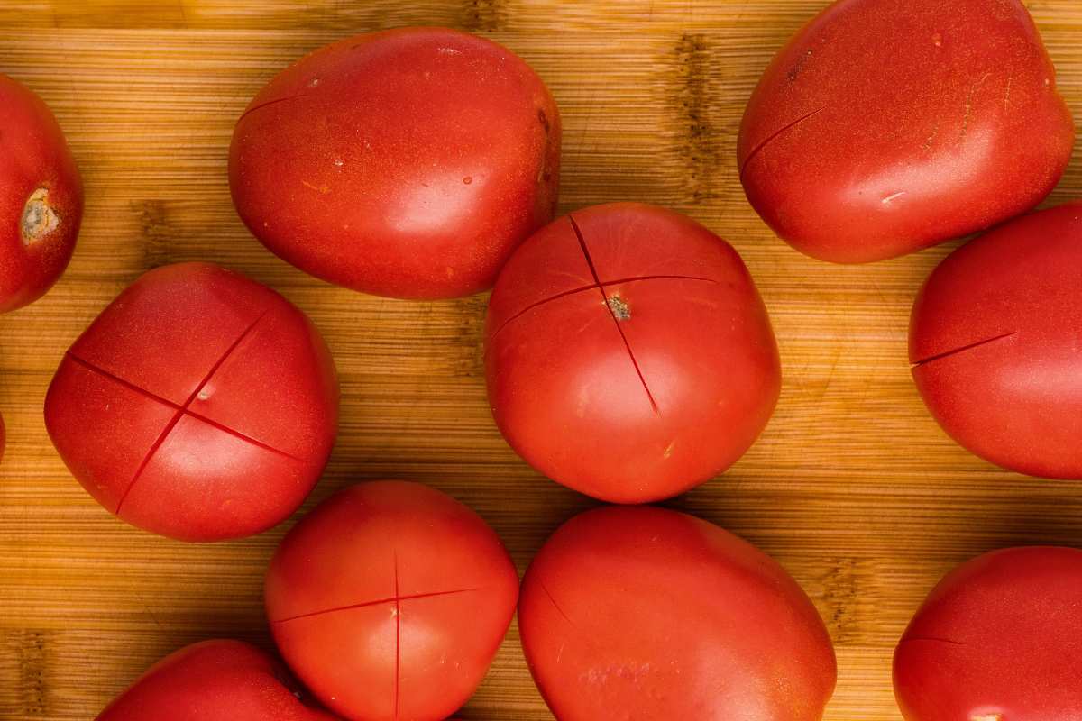 scored tomatoes on wooden cutting board.
